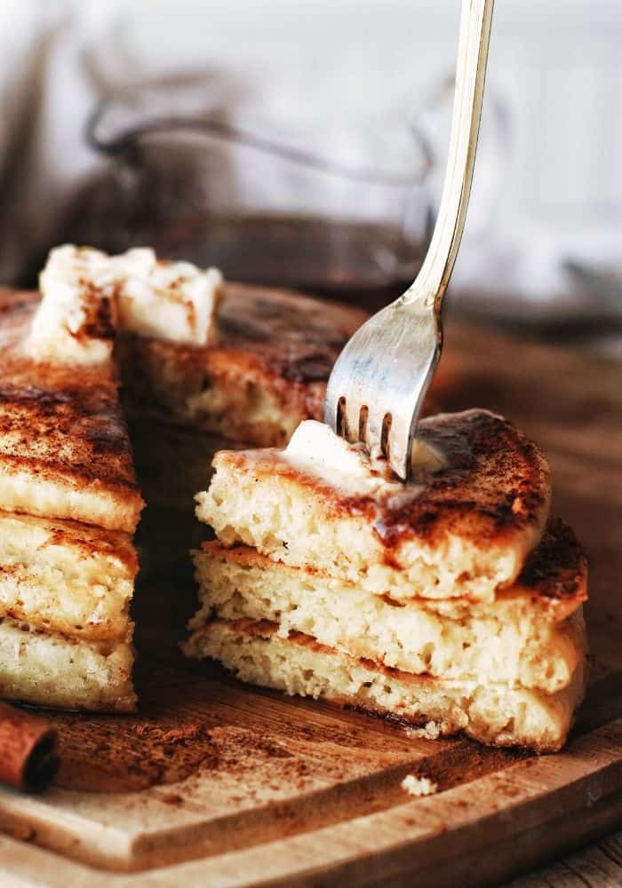 stack of pancakes with cinnamon sticks and a fork taking a slice out