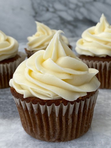 carrot cake cupcakes with cream cheese frosting on a marble countertop