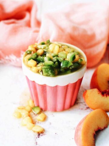 jalapeno and peach salsa in a cute pink cup with peach slices around it