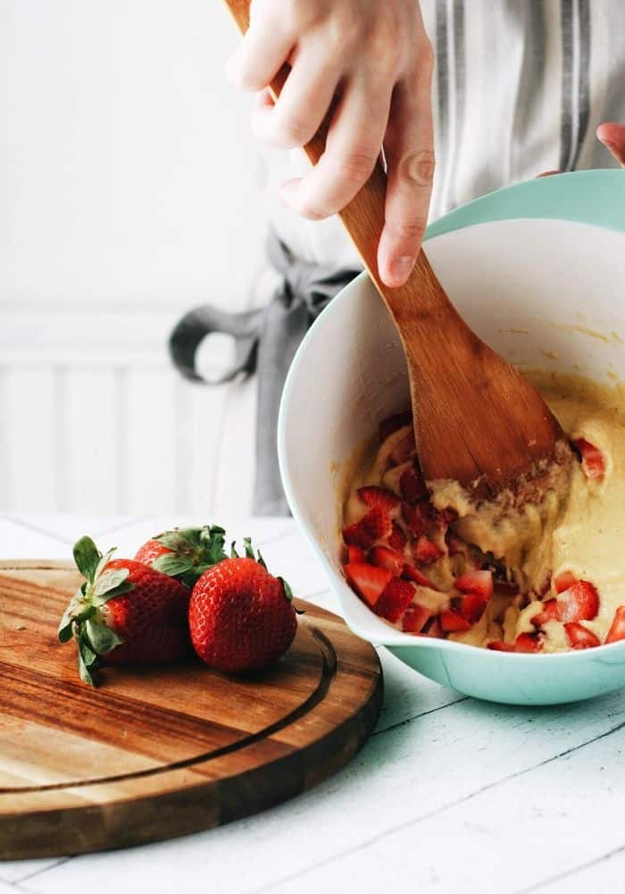 hand mixing up pancake batter with strawberries