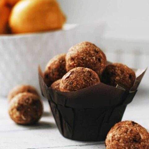 a muffin liner with lemon oat energy balls in it and lemons in the background
