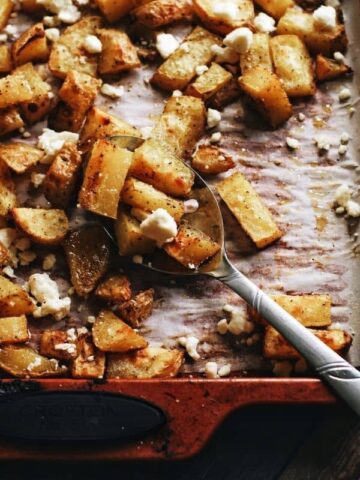 overhead shot of a spoon scooping up crispy roast potatoes on a baking sheet