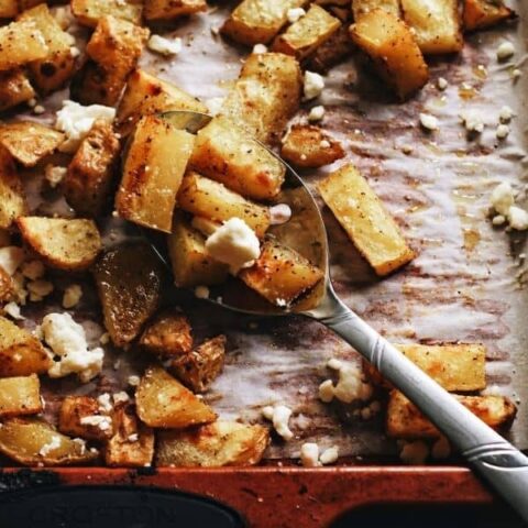 overhead shot of a spoon scooping up crispy roast potatoes on a baking sheet