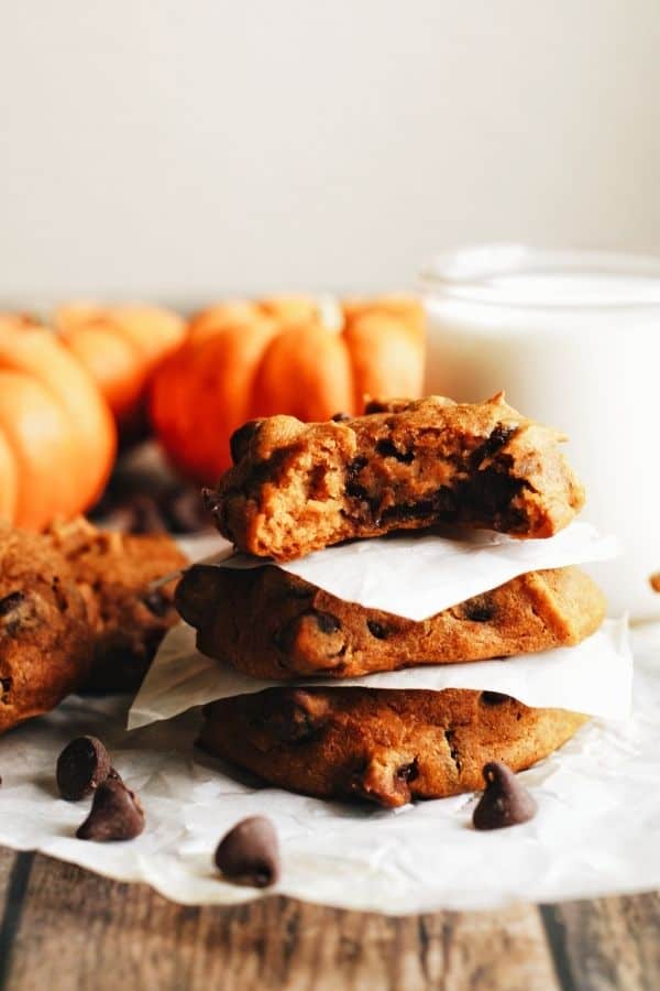 a stack of pumpkin chocolate chip cookies with pumpkins in the background