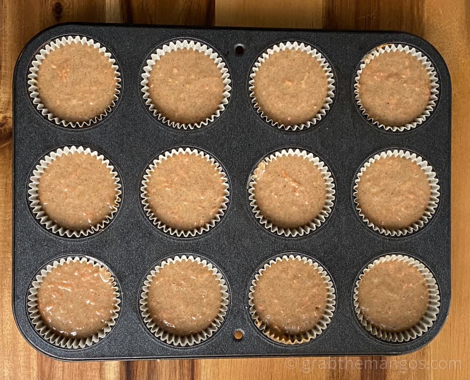 carrot cake cupcakes in a muffin tin with muffin tin liners on a cutting board 