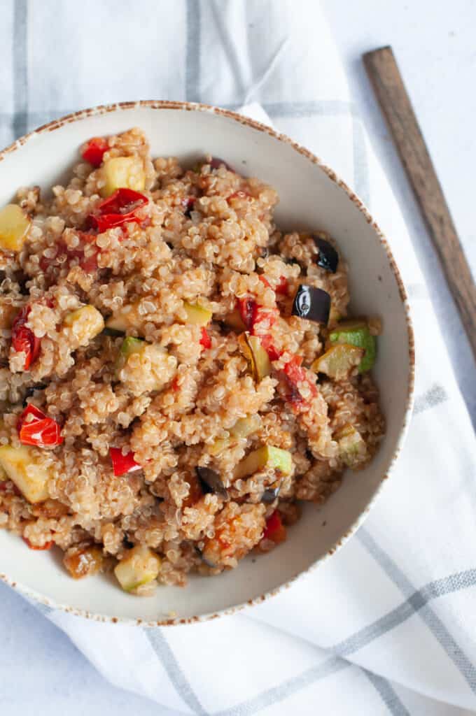 Quinoa in a bowl with vegetables and a wooden spoon to the right side. 