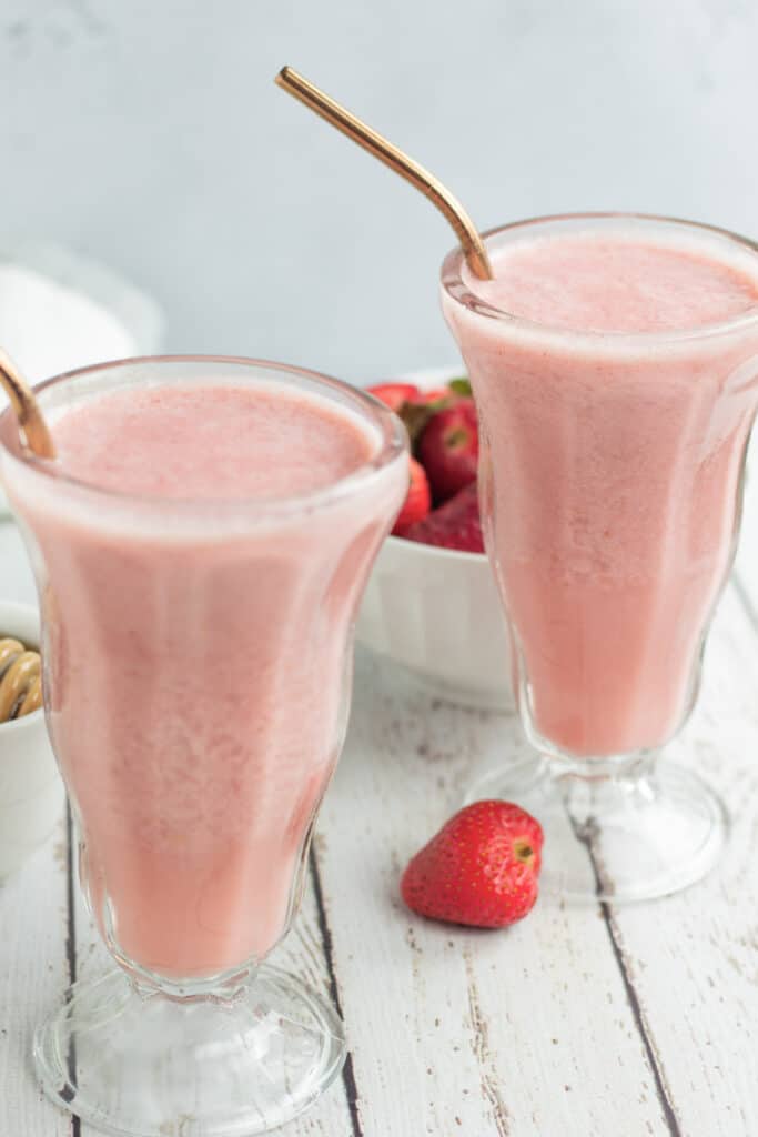 close up of two strawberry smoothies in glass with strawberries on table 