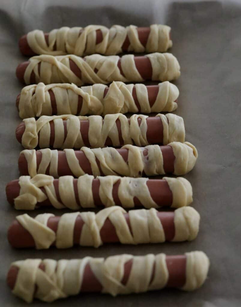 hotdogs wrapped in the crescent roll dough on parchment lined baking sheet 