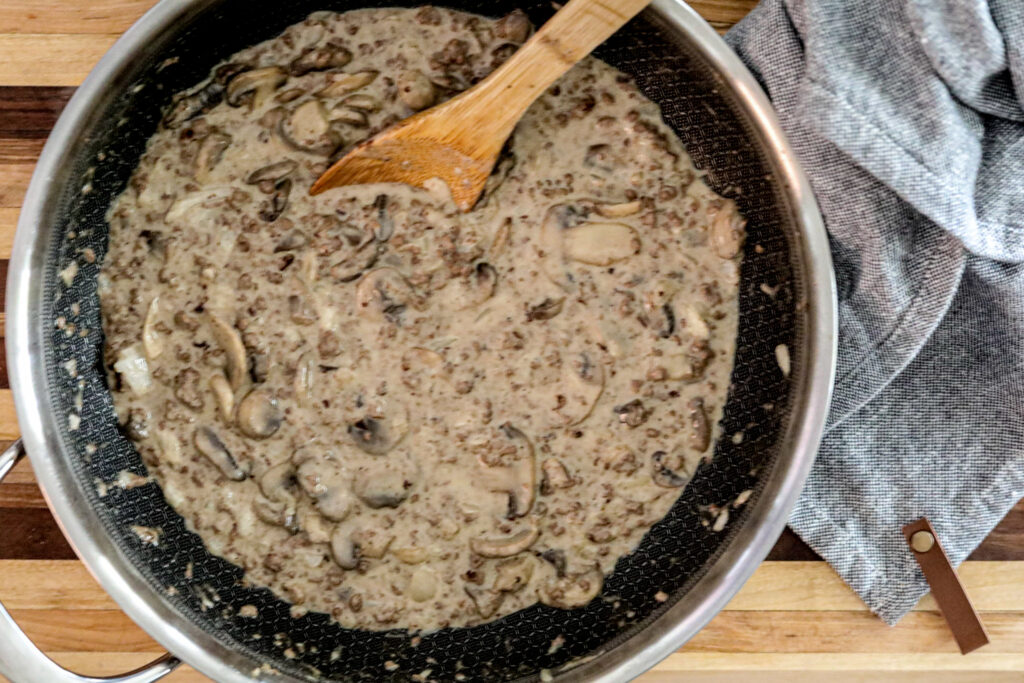 top view of beef stroganoff in a pan with a wooden spoon on a wood cutting board