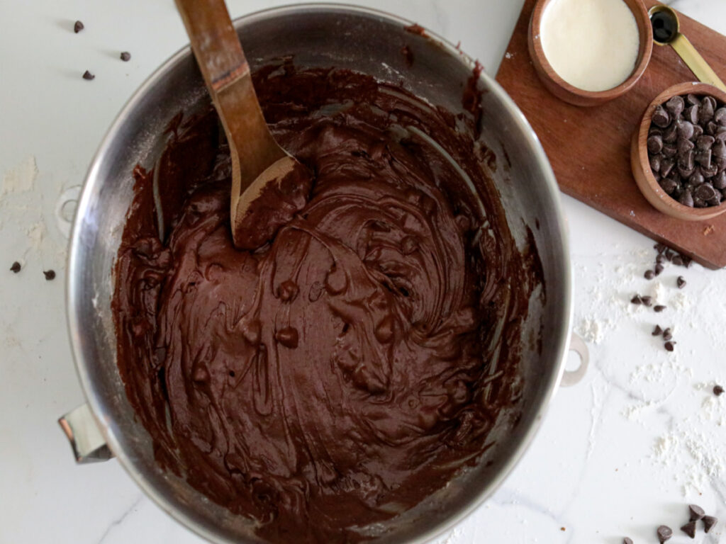 close up of brownie batter in a metal bowl with a wooden spoon
