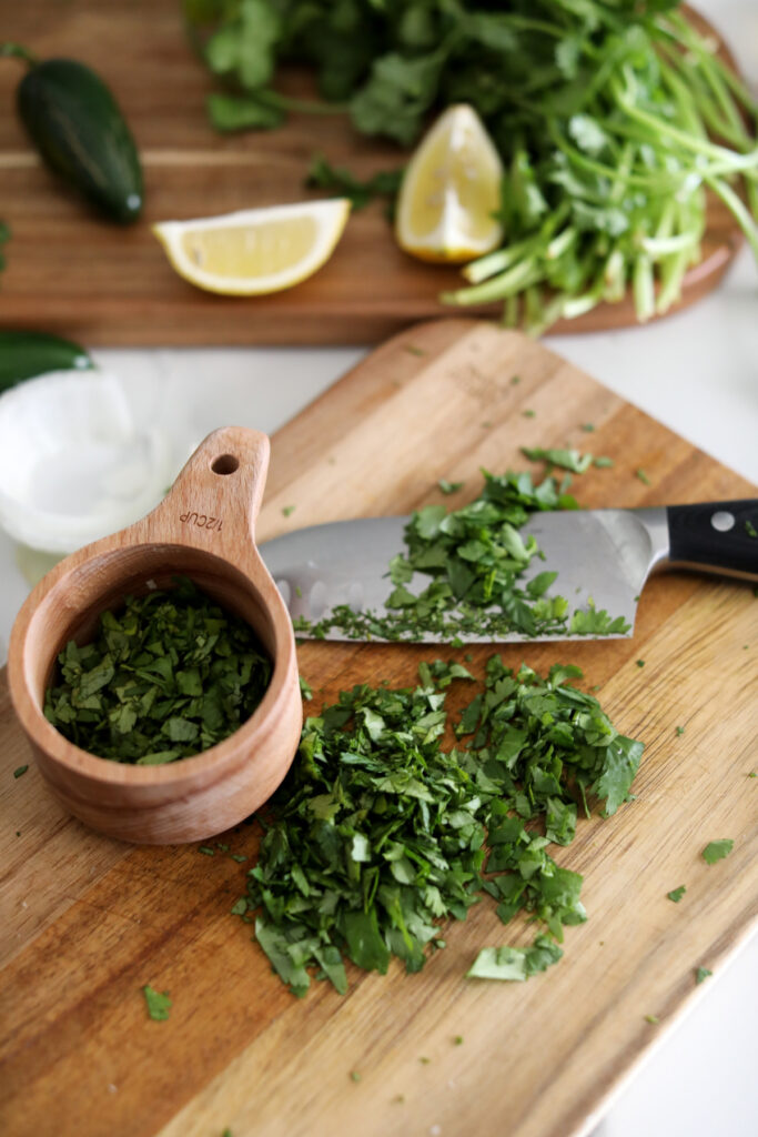 chopped cilantro on a wood cutting board with a measuring cup and knife