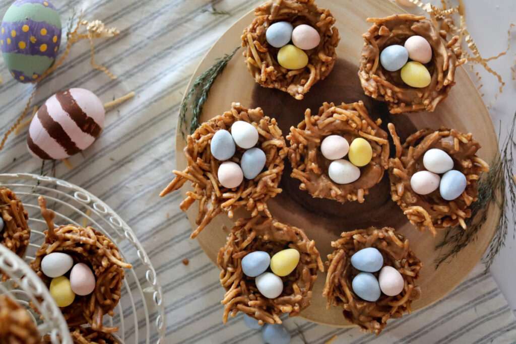 above photo of bird nest cookies on a round wood serving tray with fake easter eggs to the left